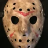 A close-up image of the Friday the 13th 2009 mask, showcasing its weathered, gritty texture, red accents, and black elastic straps against a dark background.