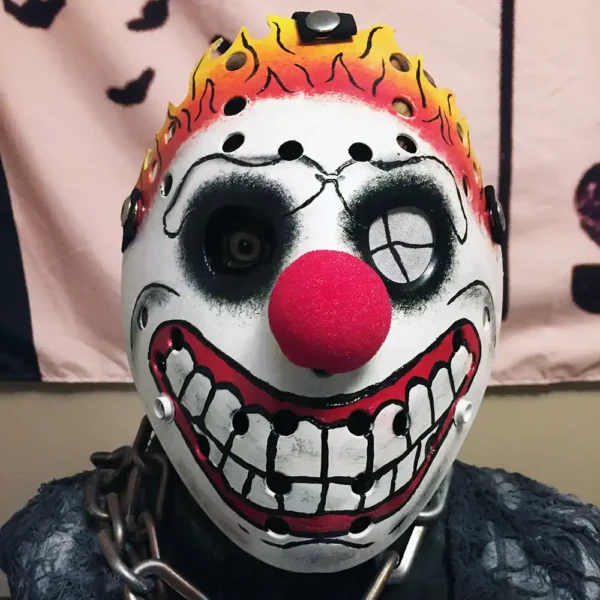 Hand-crafted Sweet Tooth Clown Mask with fiery orange-and-yellow flames, white base, red clown nose, and red smile, set against a studio background.